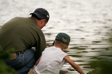 Father and son fishing together beside a quiet forest lake
