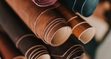 Leather bags, cases, and rolled leather hides arranged in a field-style collage for a Deutsche Optik leather care guide.